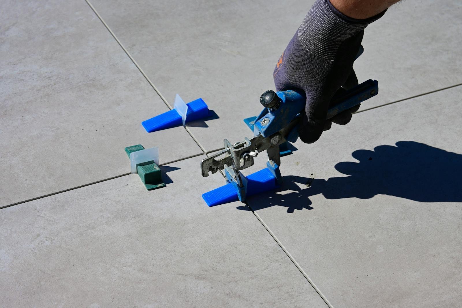 A gloved hand using a leveling tool to install tiles with spacers.