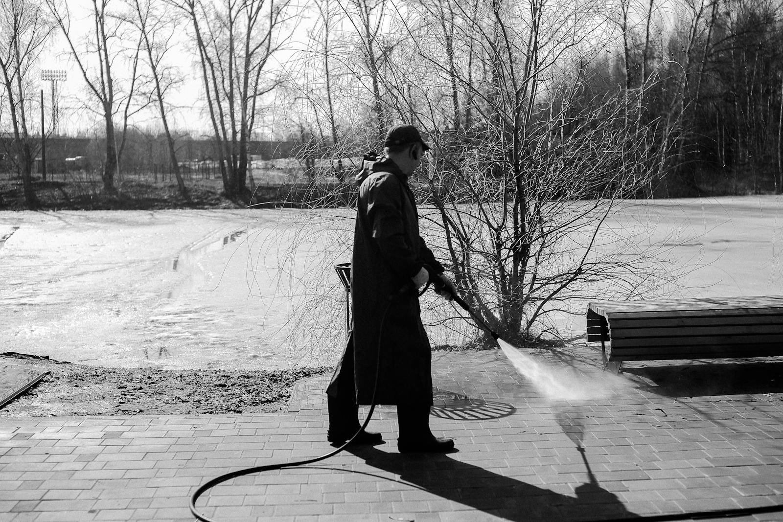 A man pressure washing pavement in a winter landscape captured in black and white.