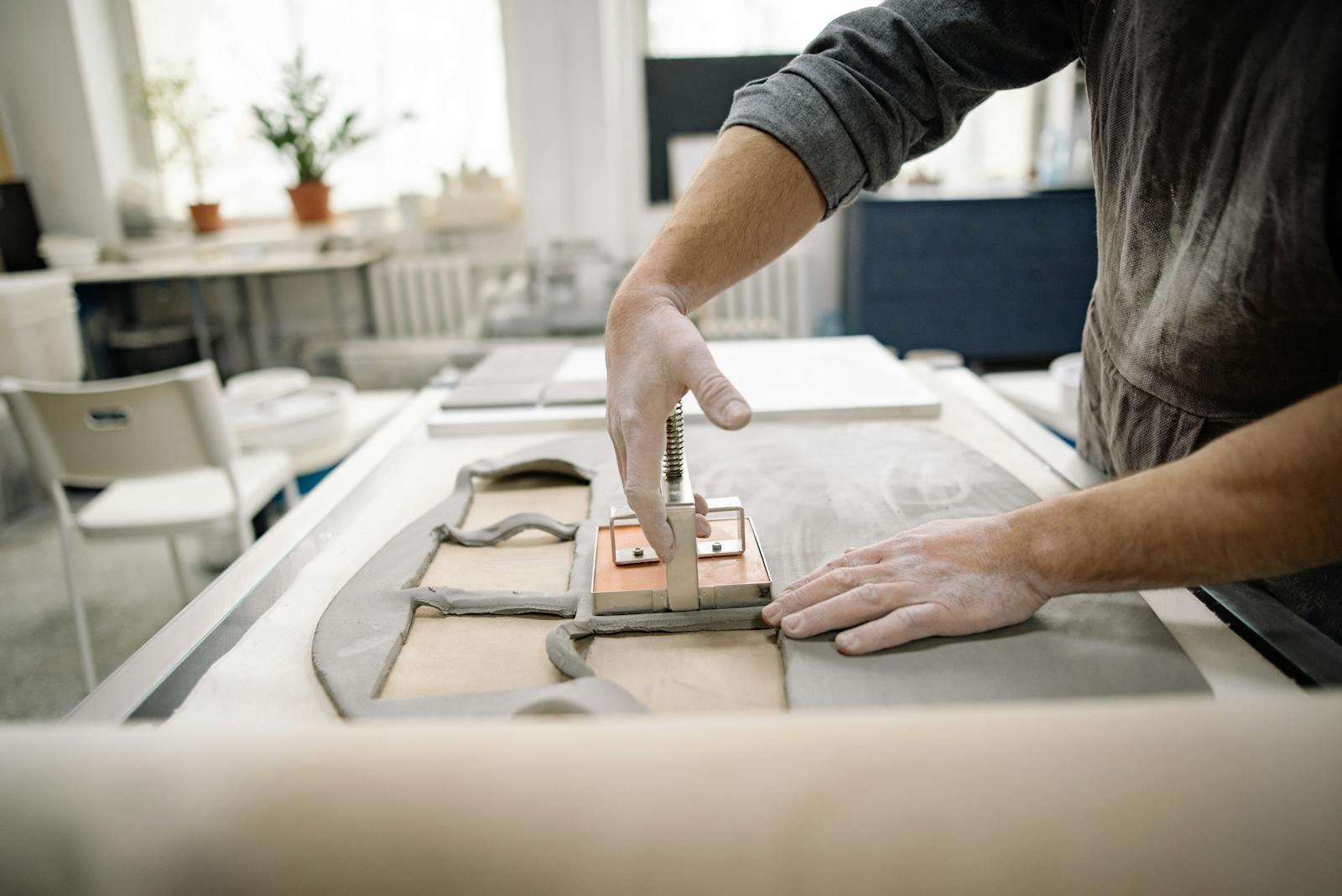 Artist crafting clay tiles with precision and skill in a sunlit studio.